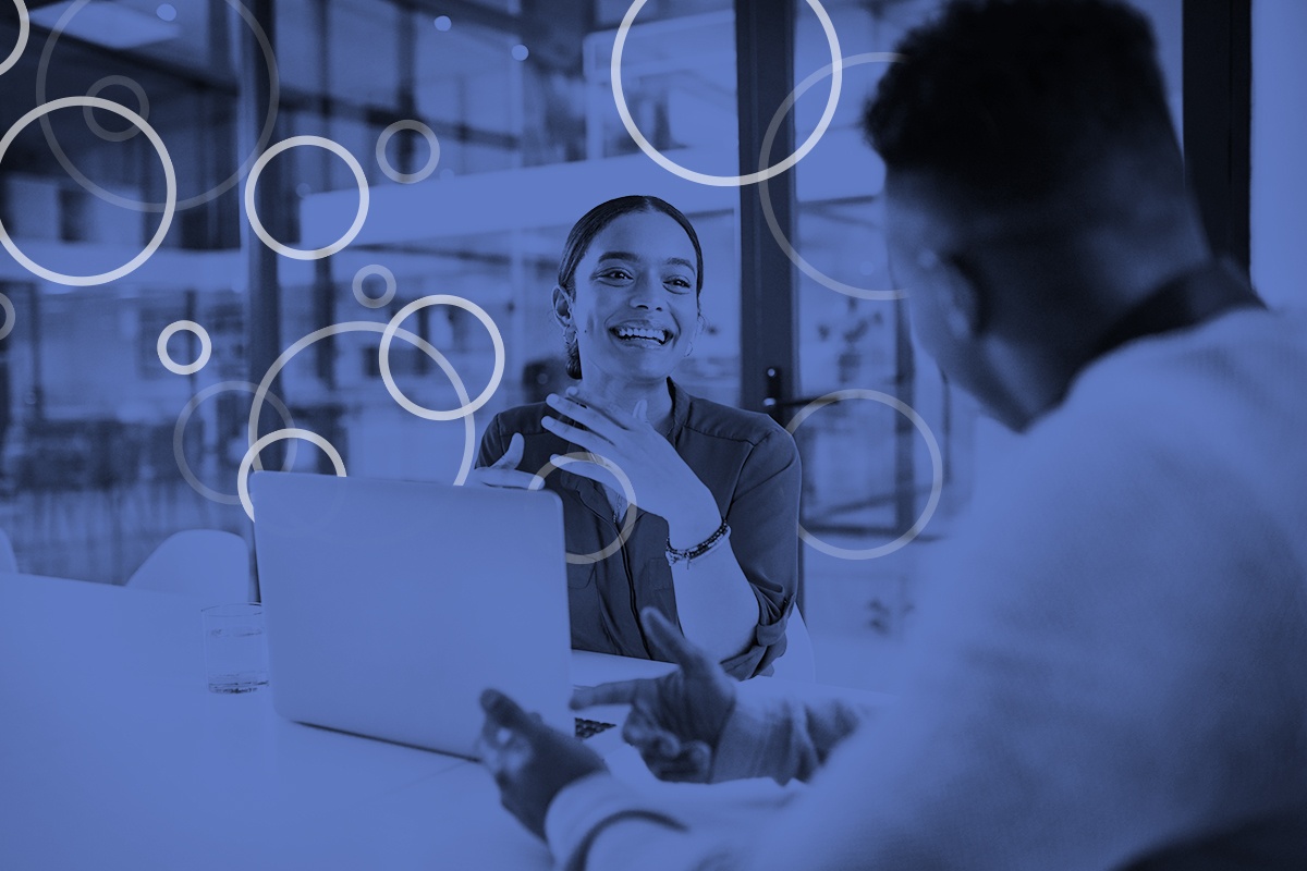 A man speaks to a smiling woman in a meeting room with data visualization circles around them, as if the data itself is coming out of a computer to join the conversation.