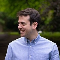 Caucasian man with brown hair wearing a blue, collared shirt, looking to his right 